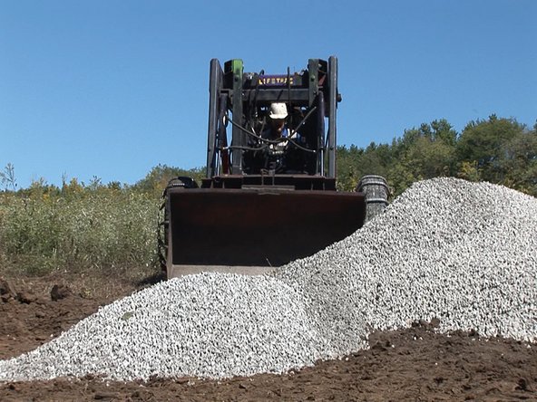 Have XX tons of gravel delivered. Make sure the truck has access to the site and has room to back up and drop the load where you want it.